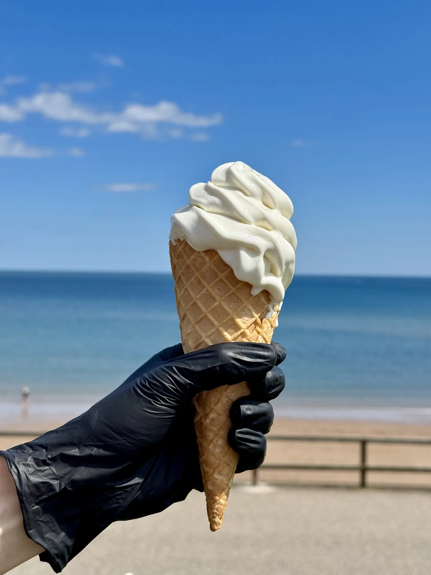 Vanilla soft serve cone held up against the beach