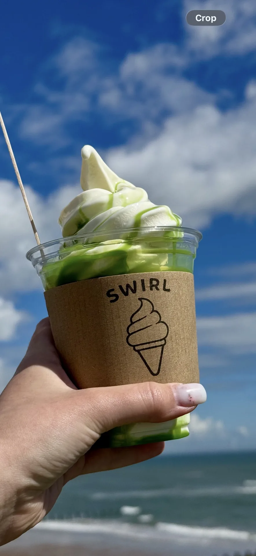 Matcha soft serve cup held up by the beach